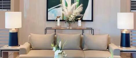 A modern living room with a beige sofa, two side tables with lamps, a coffee table with decorative items, and a large abstract painting on the wall.