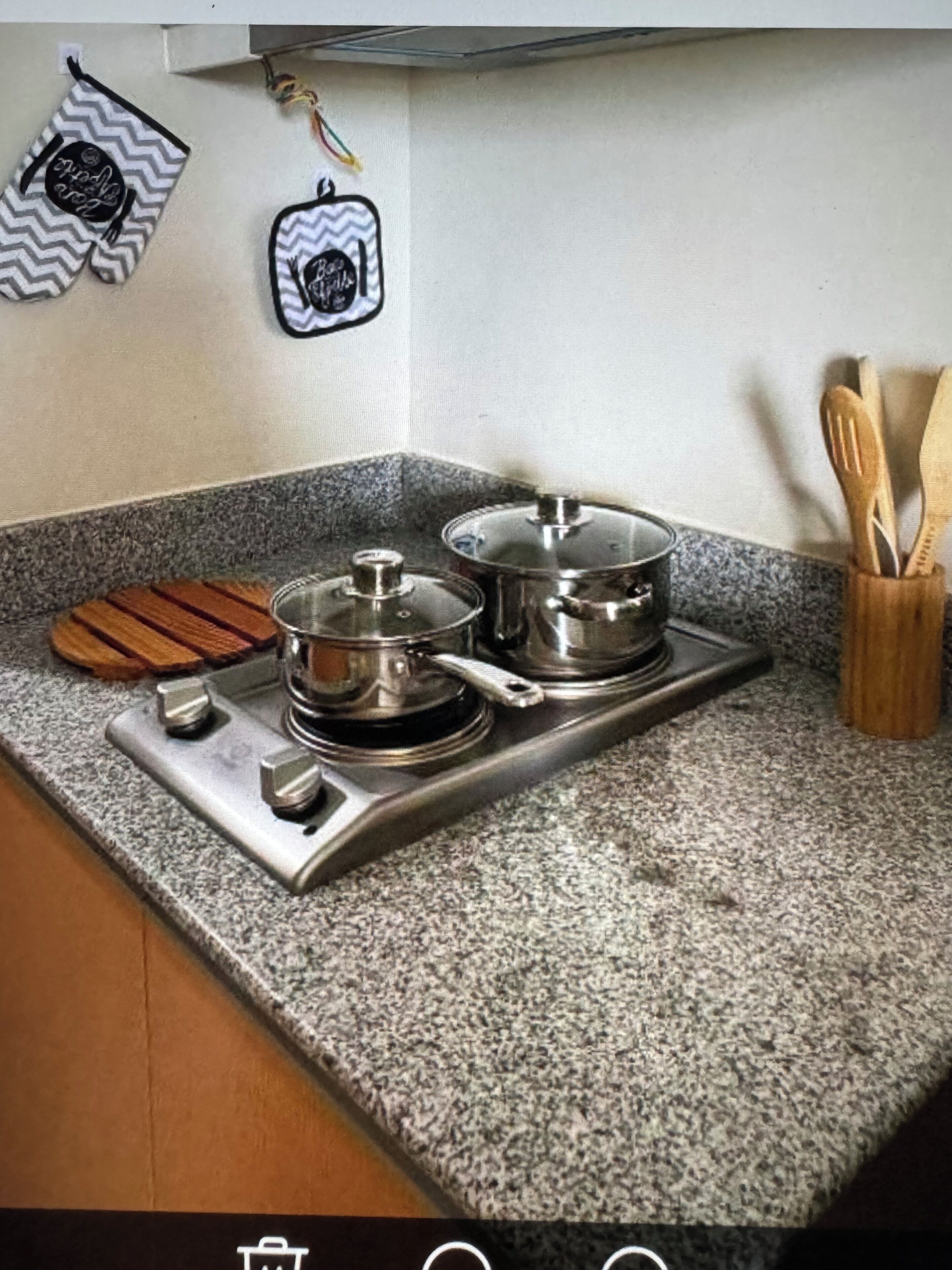 A kitchen with a granite countertop, two stainless steel pots on an induction cooktop, wooden cutting boards, and a utensil holder.