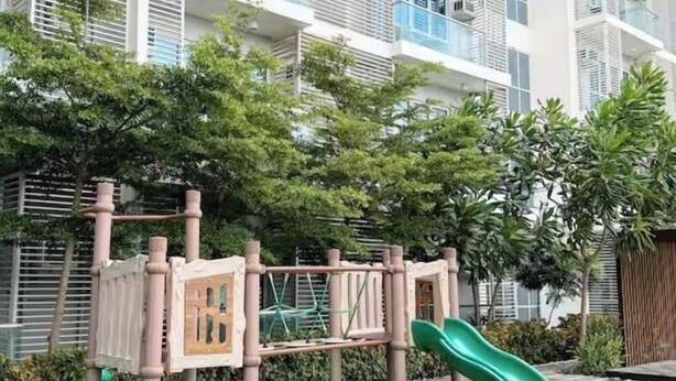 Un parque infantil con tobogán y estructuras de escalada, rodeado por un edificio de varios pisos con balcones y áreas verdes.