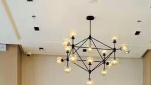 Ein modernes Wohnzimmer mit einer Couch, einem Couchtisch und gelben Sesseln. An der Wand hängt ein großes abstraktes Gemälde und über der Sitzgruppe ein Kronleuchter.