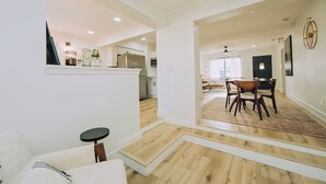 Una cucina moderna con mobili bianchi, un frigorifero e un'area pranzo con tavolo e sedie in legno.