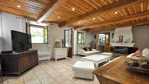 A spacious living room with a wooden ceiling, a fireplace, a television, and a dining area with a wooden table. - Amazing home in Fayence (Fayence)