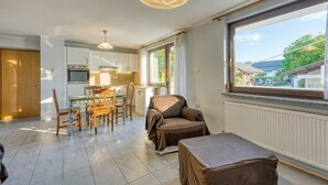 A modern kitchen with a dining area, a covered sofa, and a large window with a view.