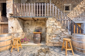 Un edificio rústico de piedra con balcón de madera, un letrero de bienvenida y una exhibición de barriles de vino.