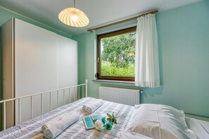 Une chambre à coucher avec un lit, une fenêtre avec des rideaux, un radiateur et un luminaire suspendu.