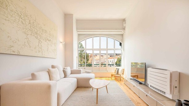 Een moderne woonkamer met een groot raam, een witte bank, een kleine tafel en een televisie.