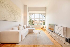 Een moderne woonkamer met een groot raam, een witte bank, een kleine tafel en een televisie.