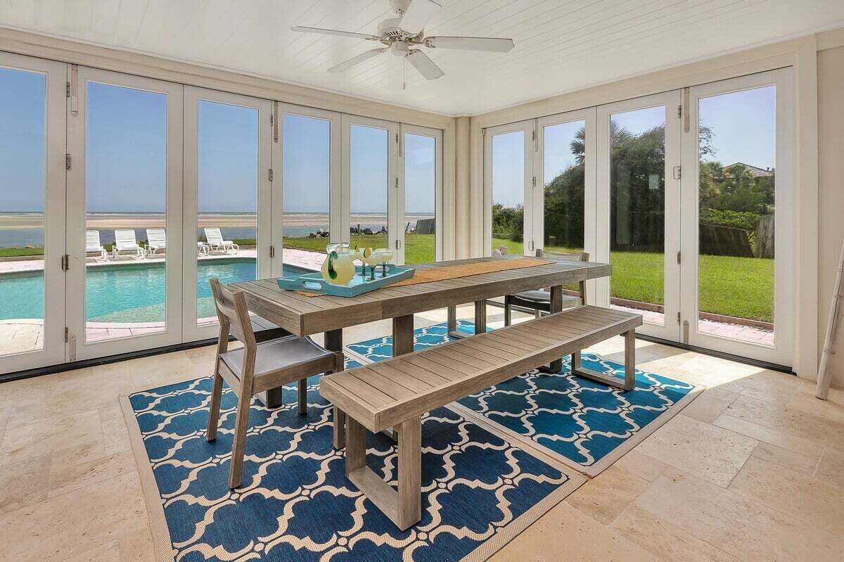 Une véranda avec vue sur la piscine, de grandes portes-fenêtres coulissantes et une table en bois avec des bancs.