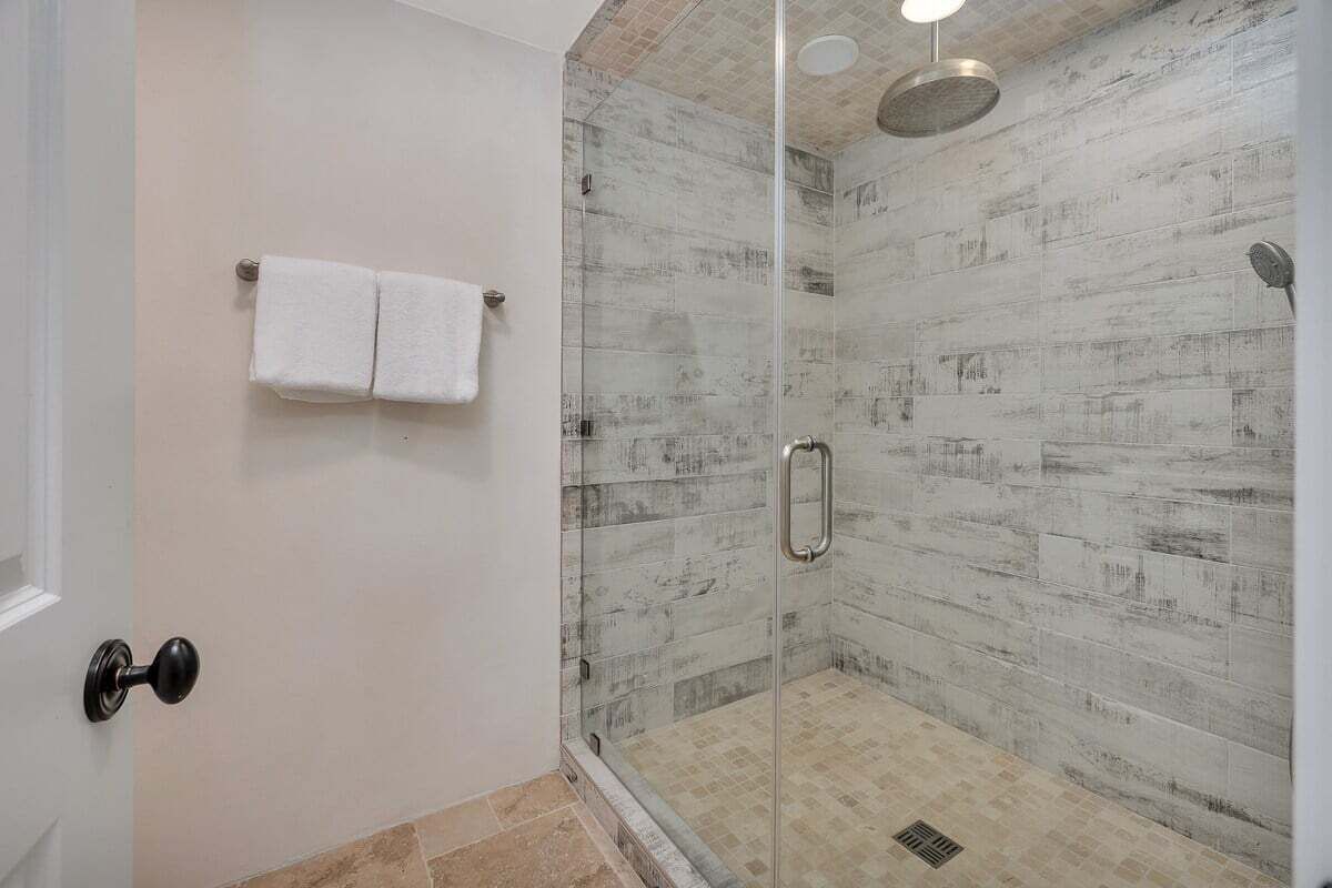 Een douche met glazen wanden, een wand met reliëfstructuur, een handdoekhouder met twee handdoeken en een deur met een ronde hendel.