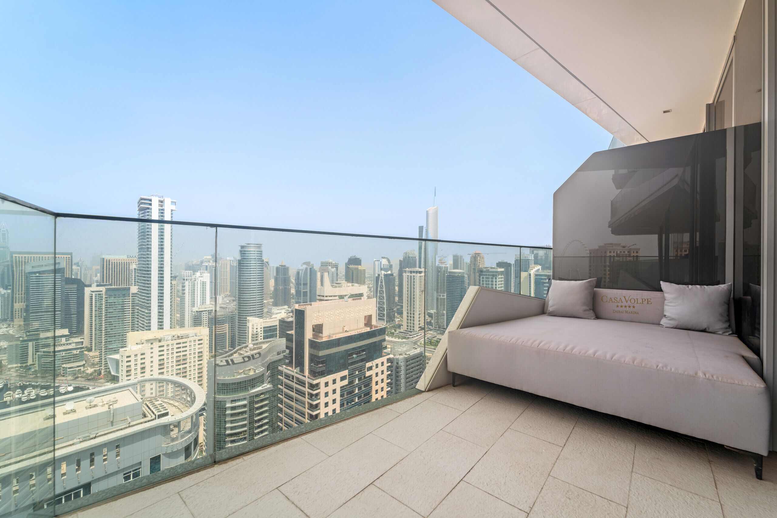 A balcony with a sofa and a glass railing overlooking a cityscape.