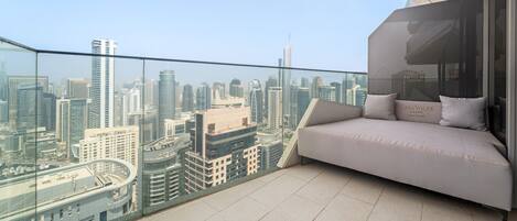 A balcony with a sofa and a glass railing overlooking a cityscape.