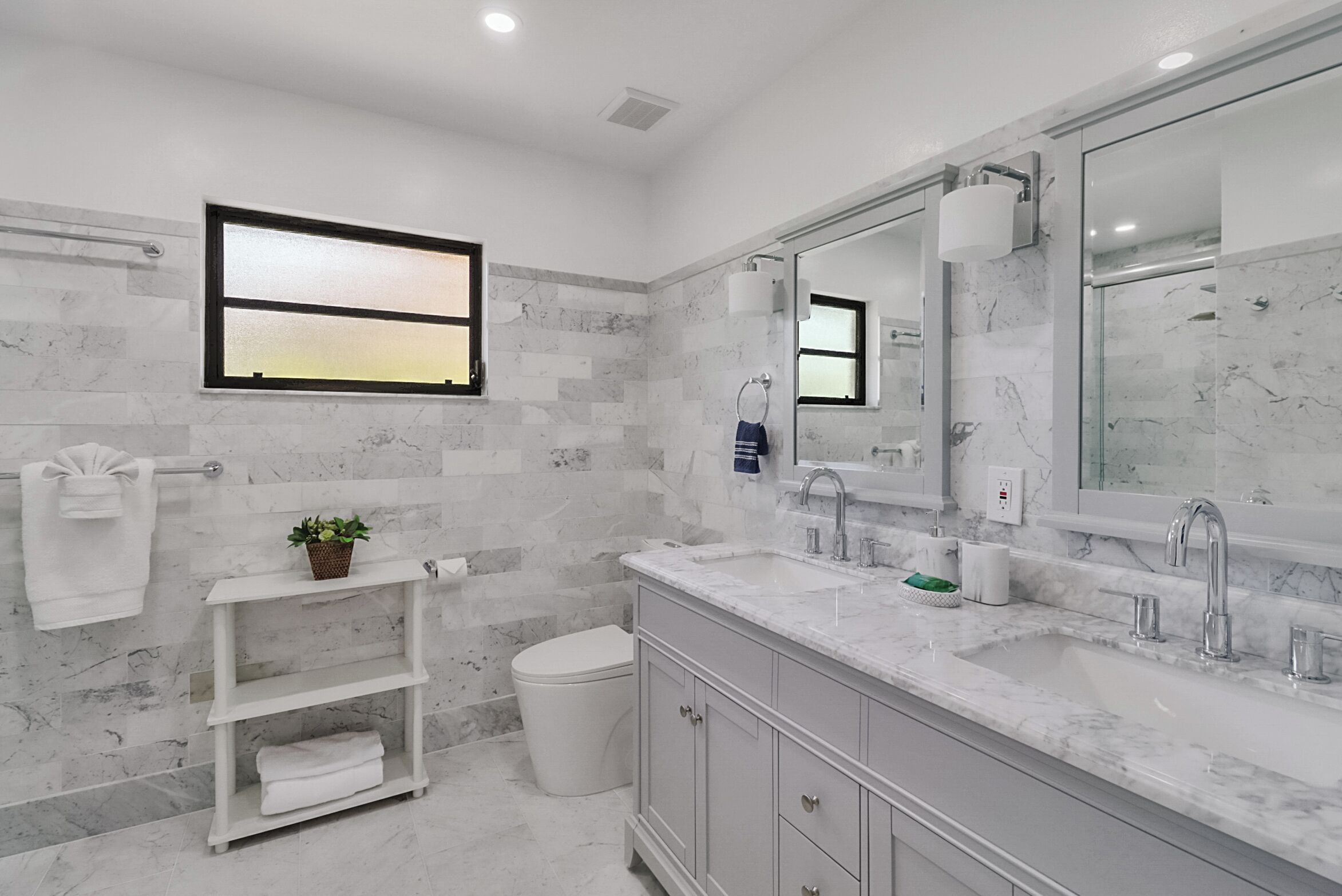 Une salle de bain moderne avec un pare-baignoire en marbre, un grand miroir, un lavabo double et des toilettes.