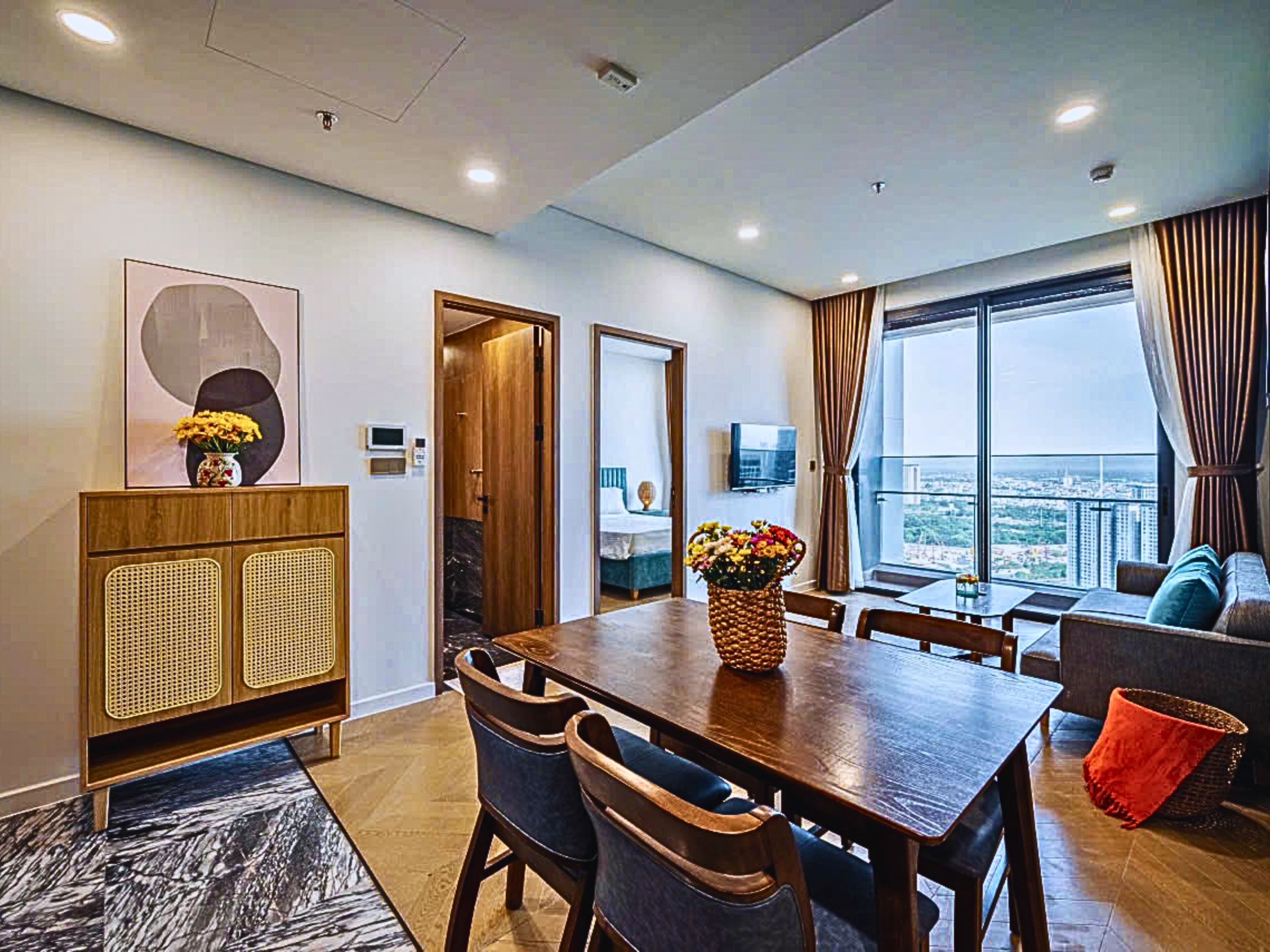 A modern living room with a wooden dining table, chairs, a sofa, and a large window offering a city view.