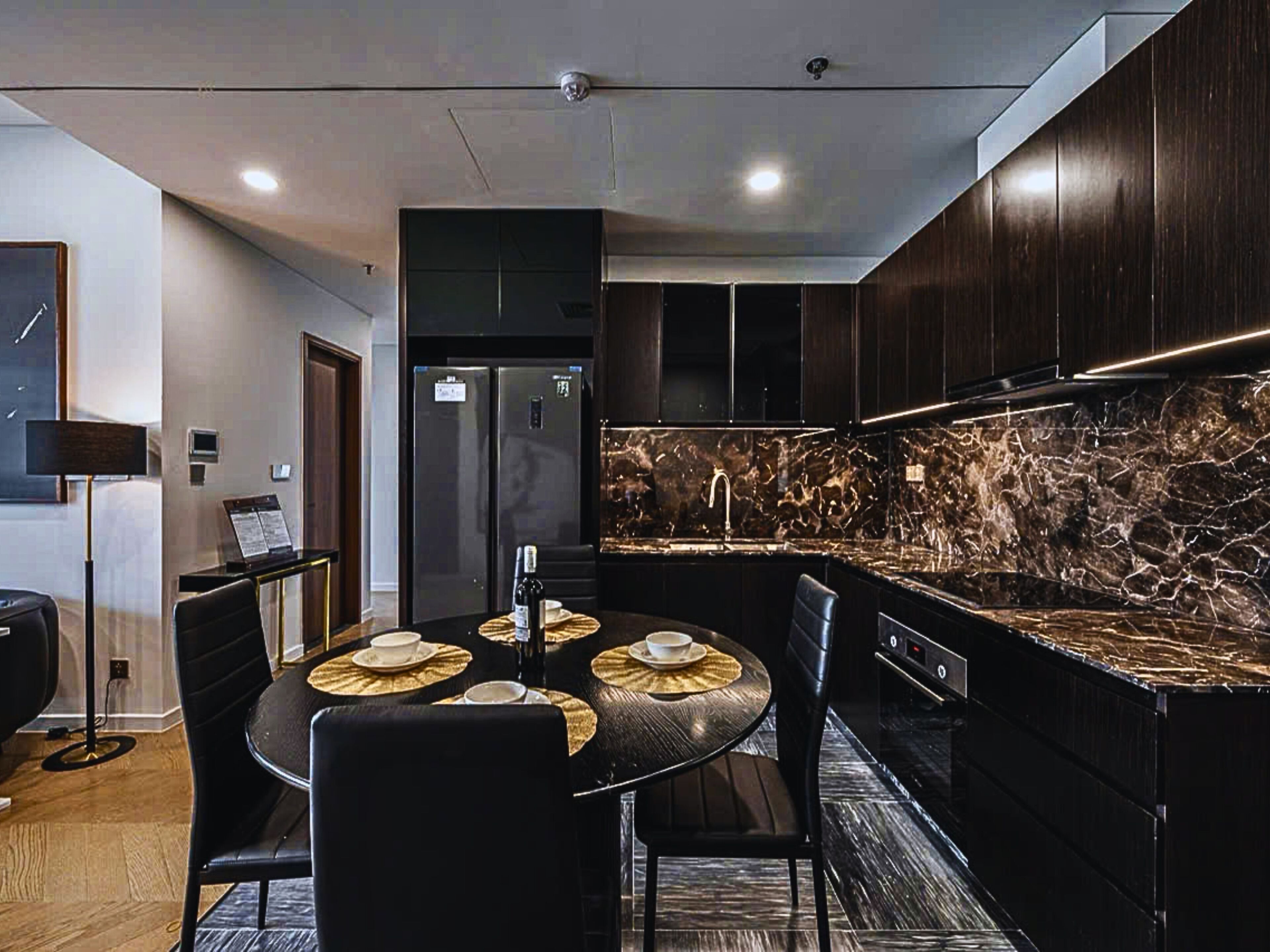 A modern kitchen with dark wood cabinets, a marble backsplash, and a dining area with a round table and chairs.