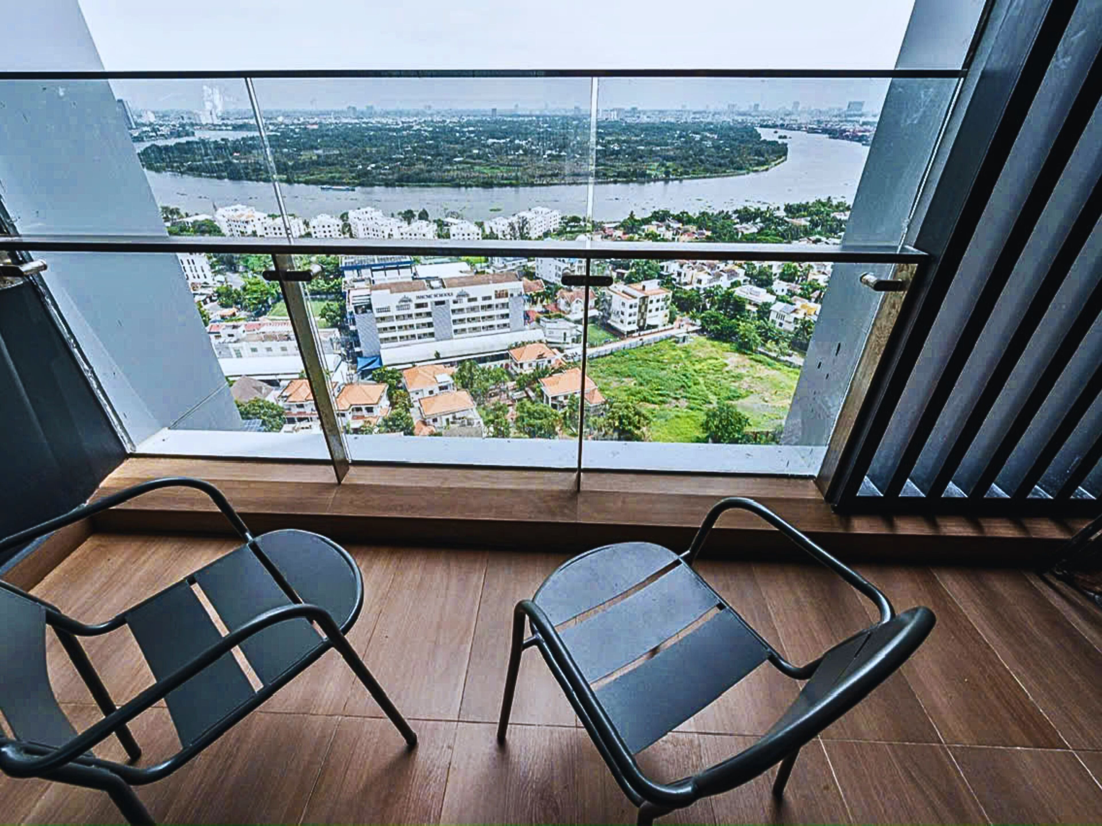 A balcony with two black chairs and a view of a river and buildings.