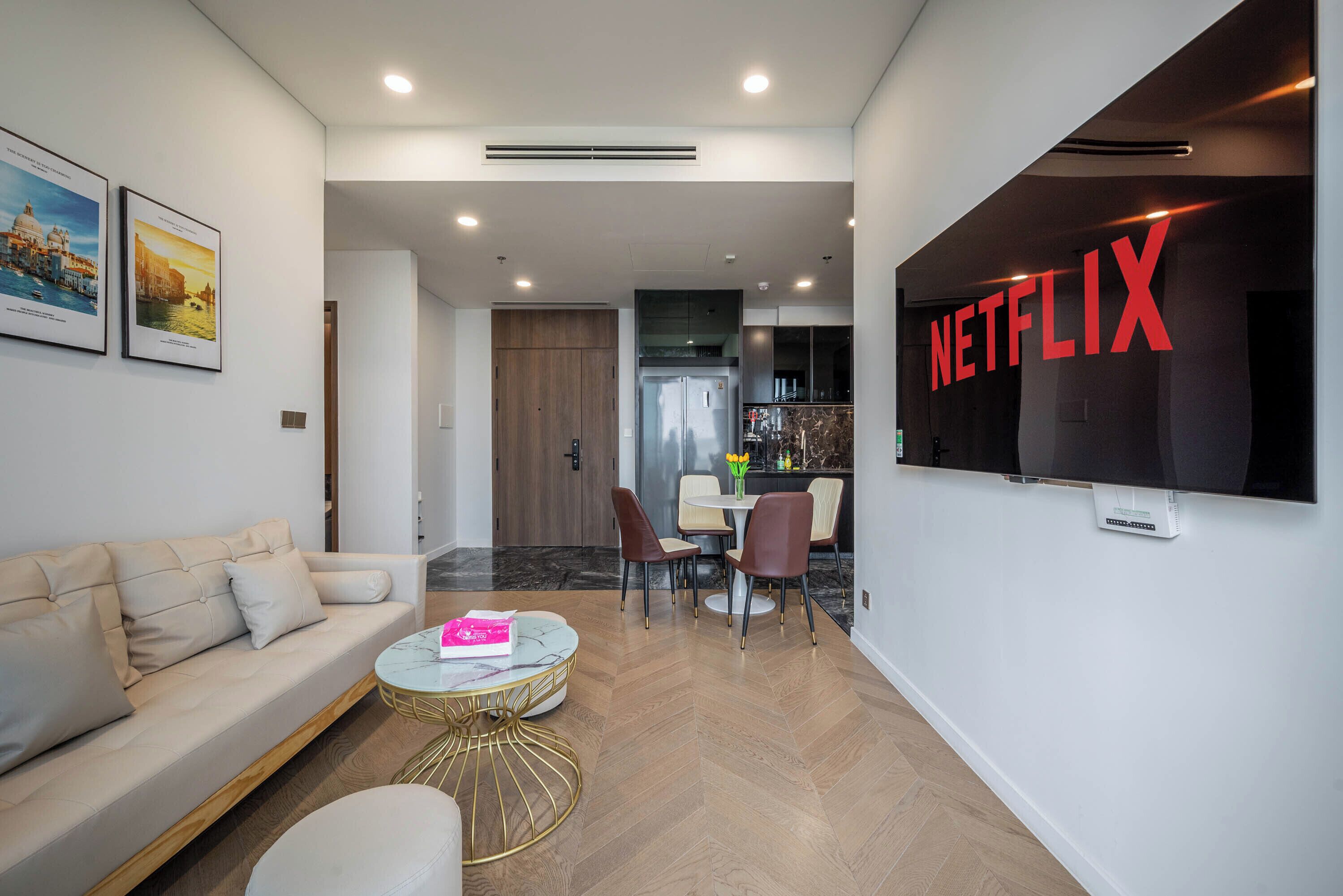 Un salon moderne avec un canapé, une table basse et un coin repas. Un grand écran de télévision affiche le logo de Netflix.