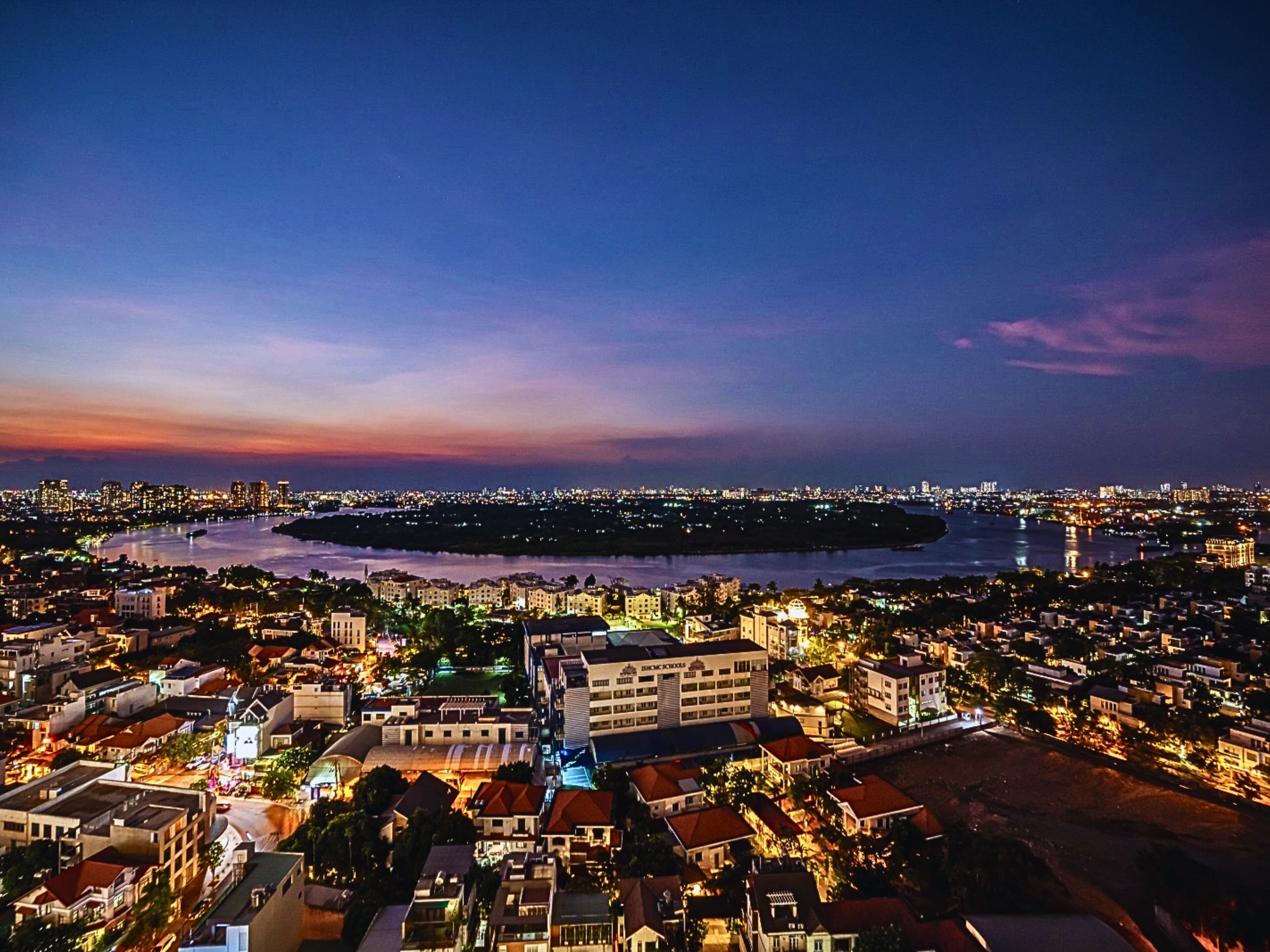 Paisagem urbana ao entardecer com um rio e um edifício grande em primeiro plano.