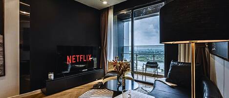 A modern living room with a large TV displaying 'NETFLIX', a sofa, a coffee table, and a view of the city through large windows.