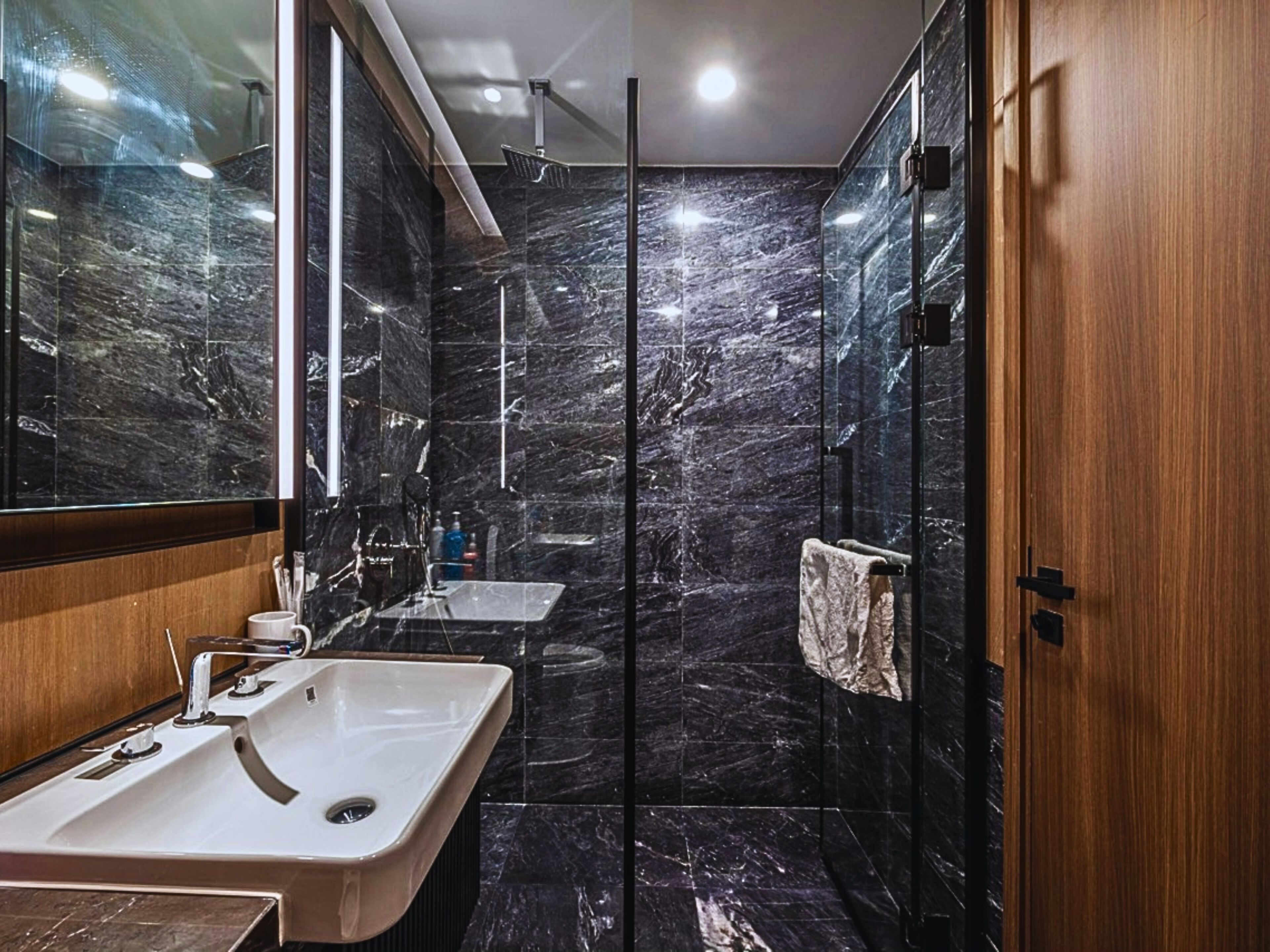 A modern bathroom with a large mirror, a sink, a shower, and a towel rack.