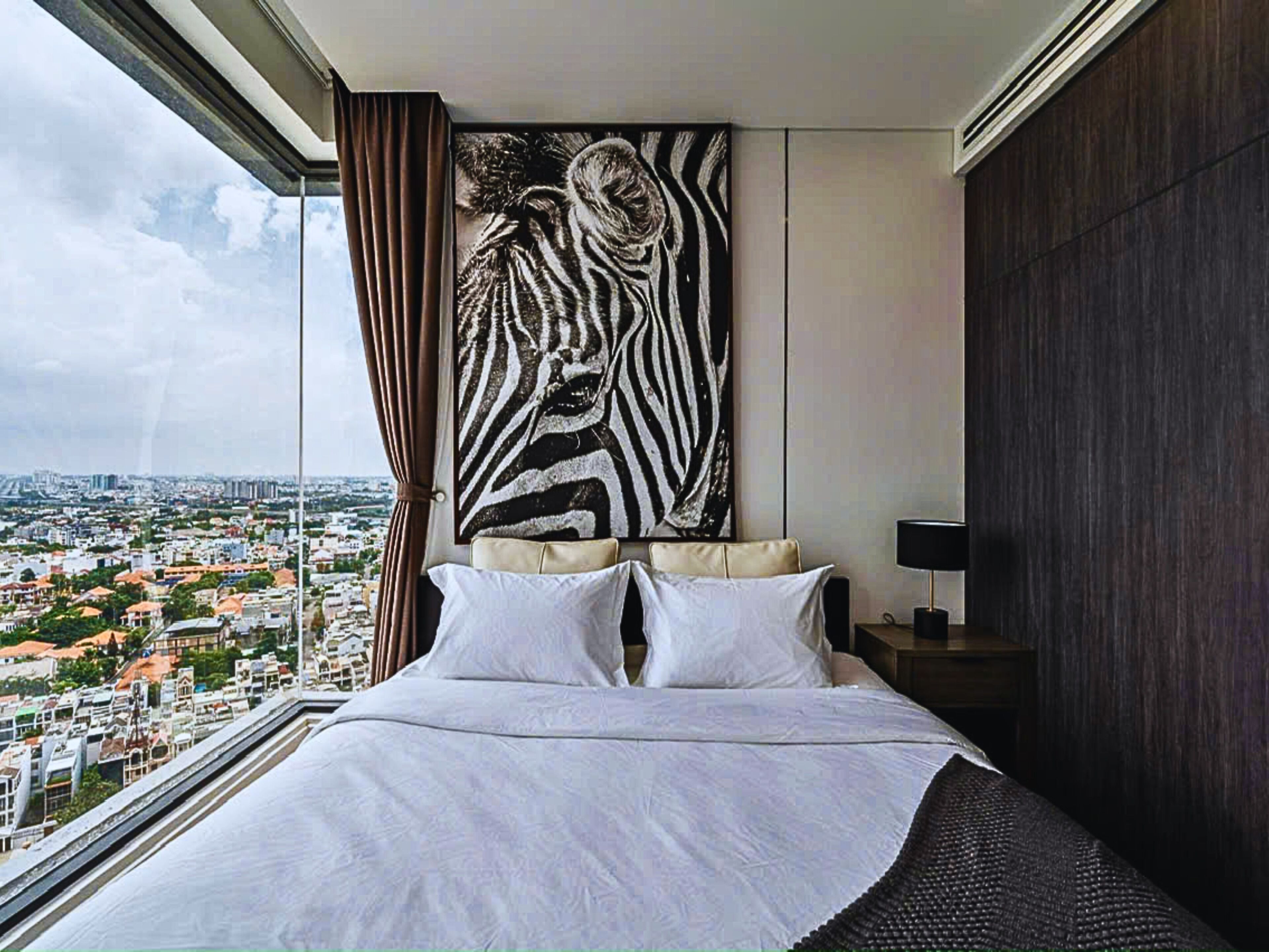 A bedroom with a large bed, a city view, and a zebra print artwork on the wall.