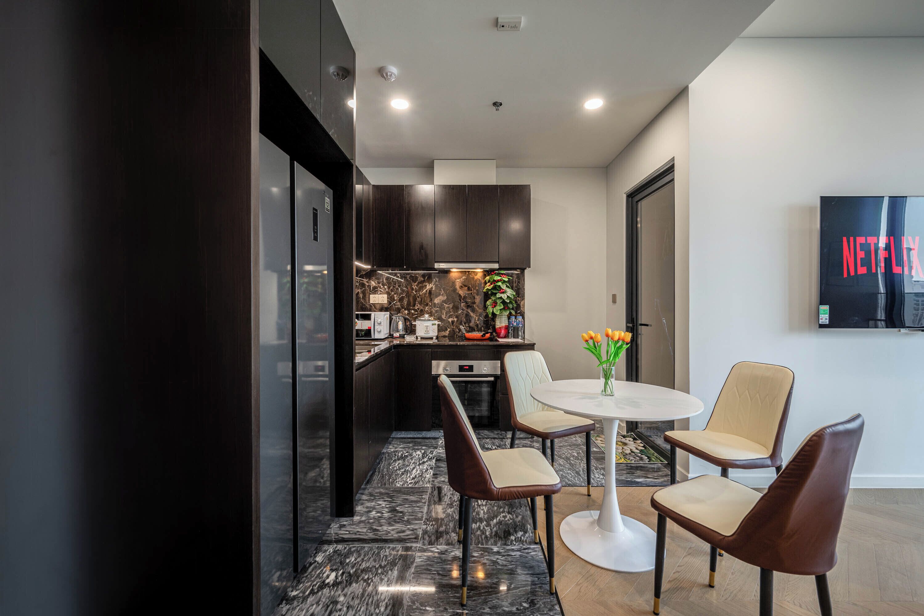 A modern kitchen with dark cabinetry, a marble backsplash, and a dining area with a white table and four chairs.