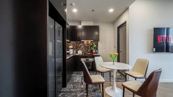 A modern kitchen with dark cabinetry, a marble backsplash, and a dining area with a white table and four chairs.