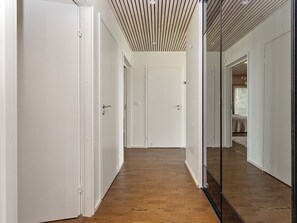 A hallway with wooden flooring, white doors, and a glass partition reflecting the room. - Villa kirsikka by Interhome (Hämeenlinna)