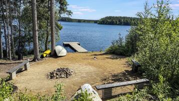 A lakeside campsite with a dock, a fire pit, and a bench.