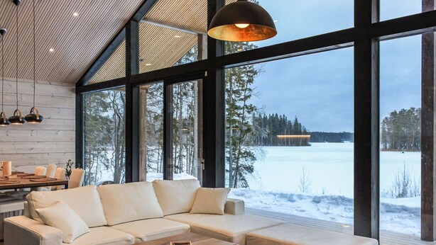 Moderni olohuone, jossa on kulmasohva, puinen sohvapöytä ja suuret ikkunat, joista avautuu näkymä lumiseen maisemaan.