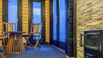 A wooden cabin interior with a fireplace, two doors leading outside, and a table with chairs.