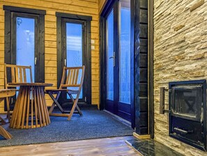 Interior de una cabaña de madera con chimenea, dos puertas que dan al exterior y una mesa con sillas.