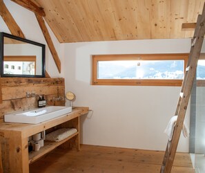 Une salle de bain en bois avec un lavabo blanc, des étagères en bois, un miroir et une fenêtre donnant sur les montagnes.
