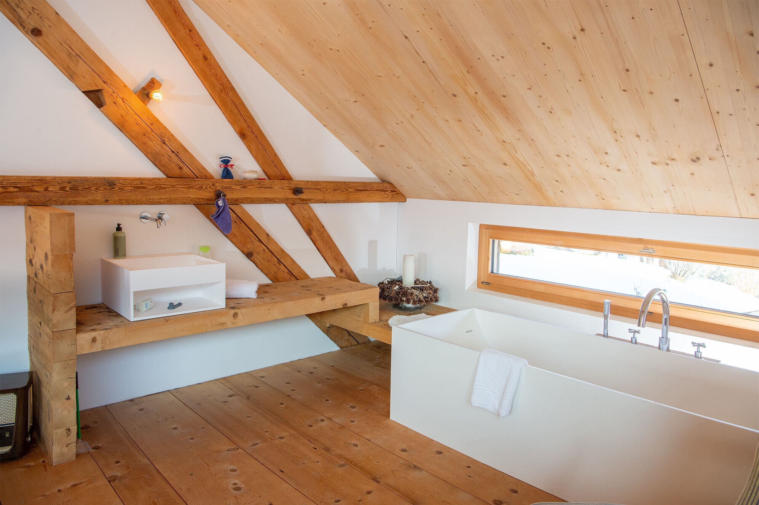 Een moderne badkamer met een houten plafond, een witte badkuip, een wastafel en een raam dat voor natuurlijk licht zorgt.
