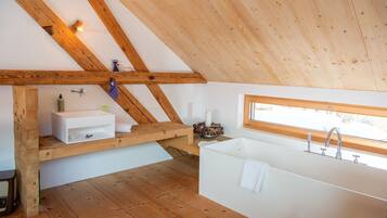 Een moderne badkamer met een houten plafond, een witte badkuip, een wastafel en een raam dat voor natuurlijk licht zorgt.