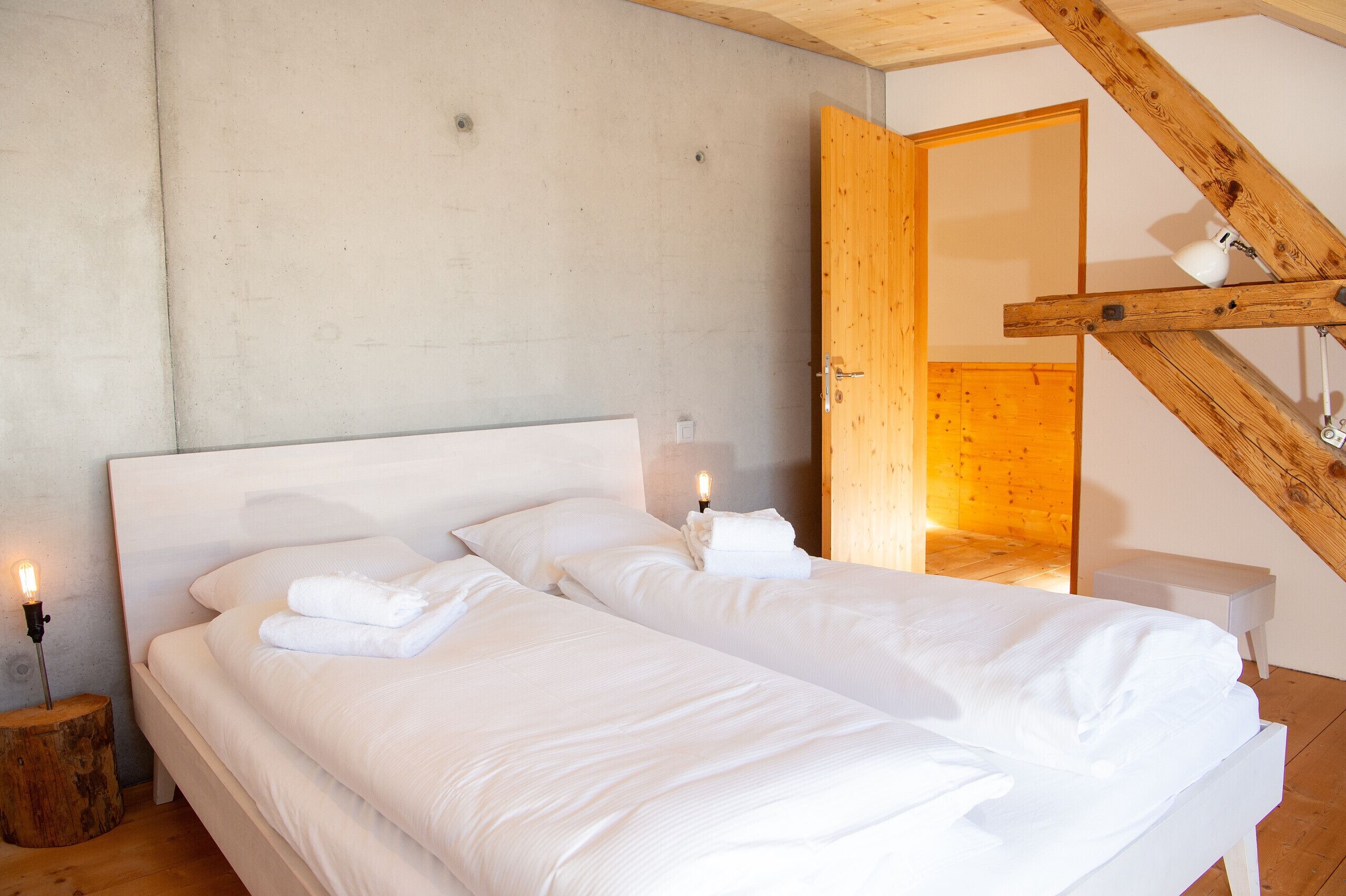 A bedroom with two beds, a wooden ceiling, and a nightstand with a lamp.