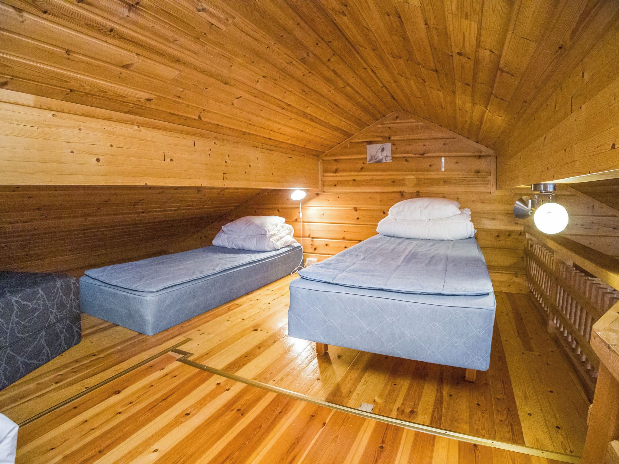 A cozy cabin with two single beds, wooden walls, and a sloped ceiling.