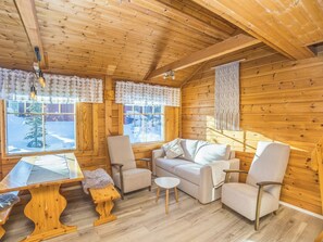 A cozy cabin interior with wooden walls, a sofa, chairs, a small table, and a window with a view of a snowy landscape. - Operomukka 5 by Interhome (Kittilä)