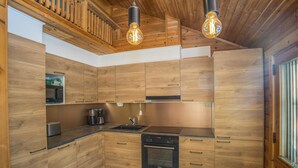 A modern kitchen with wooden cabinetry, a built-in microwave, a coffee maker, and a stove. - Operomukka 5 by Interhome (Kittilä)