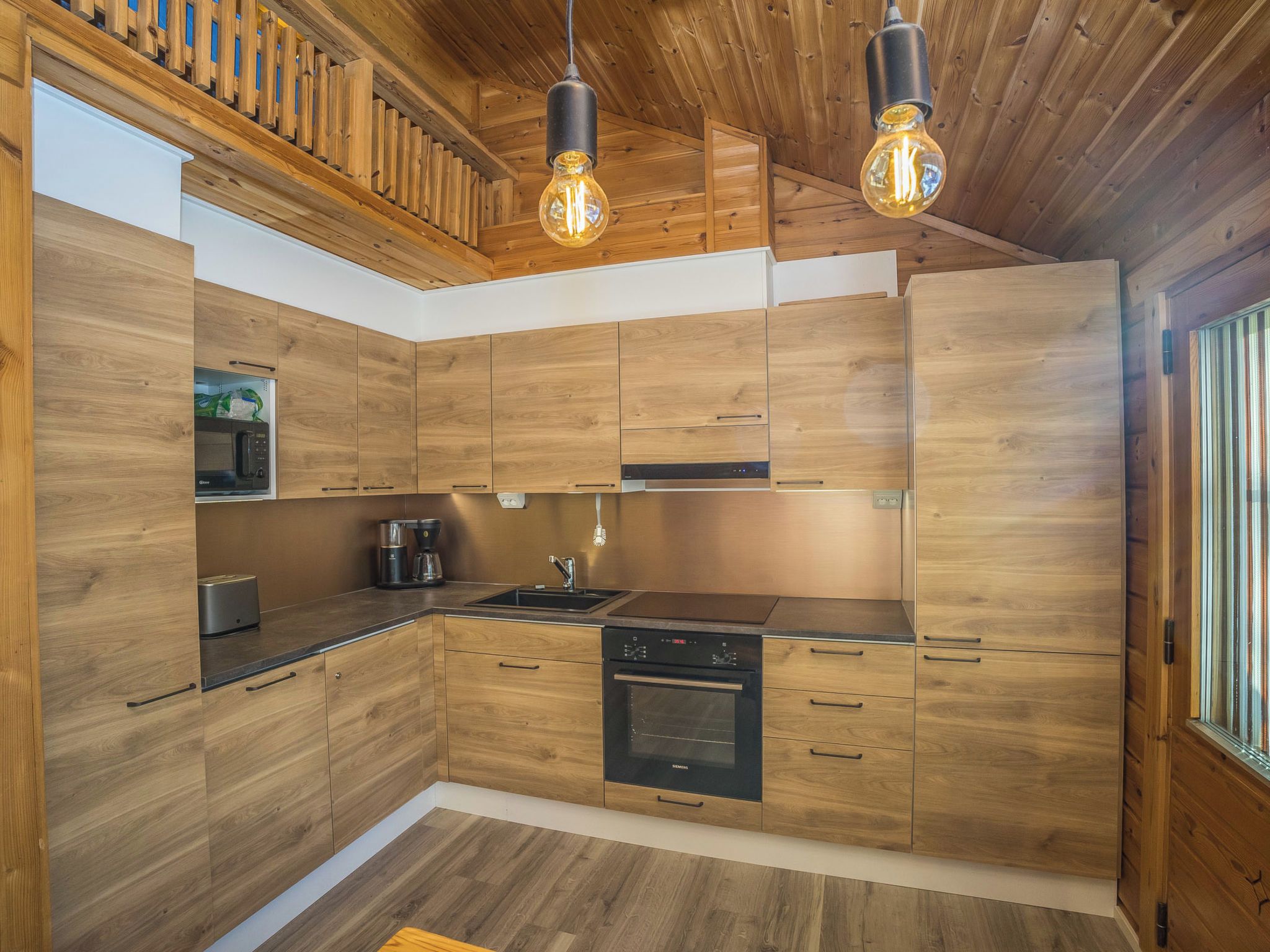 A modern kitchen with wooden cabinetry, stainless steel appliances, and pendant lighting.