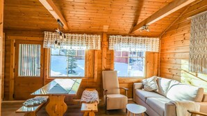 A cozy cabin interior with wooden walls and ceiling, a sofa, a chair, a small table, and two windows with curtains. - Operomukka 5 by Interhome (Kittilä)