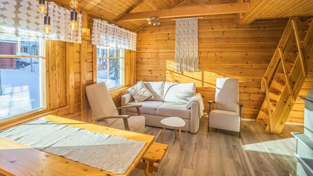A cozy cabin interior with a wooden ceiling, a sofa, two armchairs, a small table, and a window with a view of a snowy landscape. - Operomukka 5 by Interhome (Kittilä)