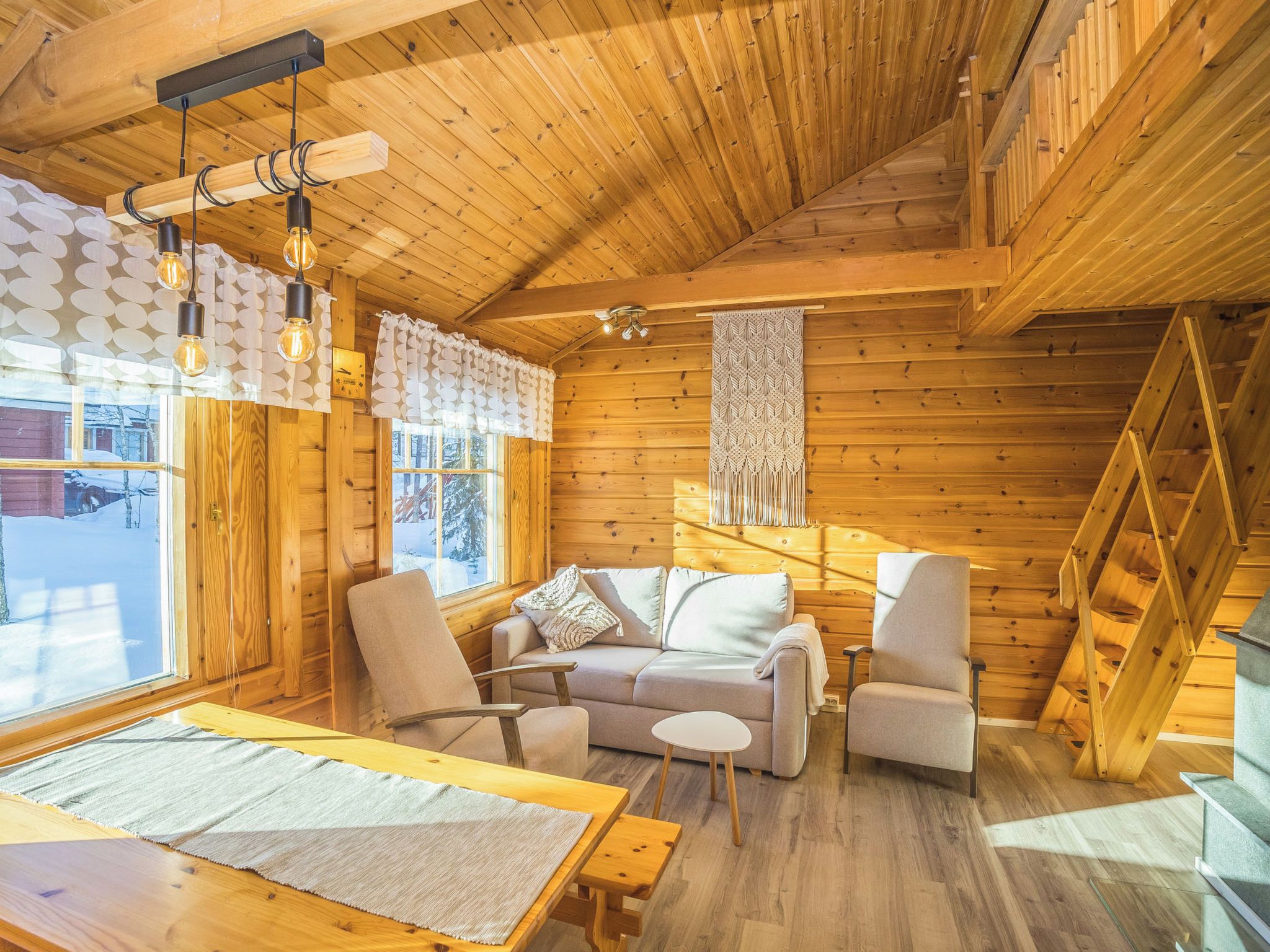 L’intérieur chaleureux d’un chalet, avec un revêtement mural en bois, un canapé, des fauteuils, une table à manger et un escalier.
