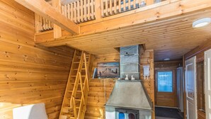 A wooden cabin interior with a fireplace, a ladder, and a chair. - Operomukka 5 by Interhome (Kittilä)