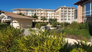 Un hotel con varios pisos, balcones y un jardín con diversas plantas.