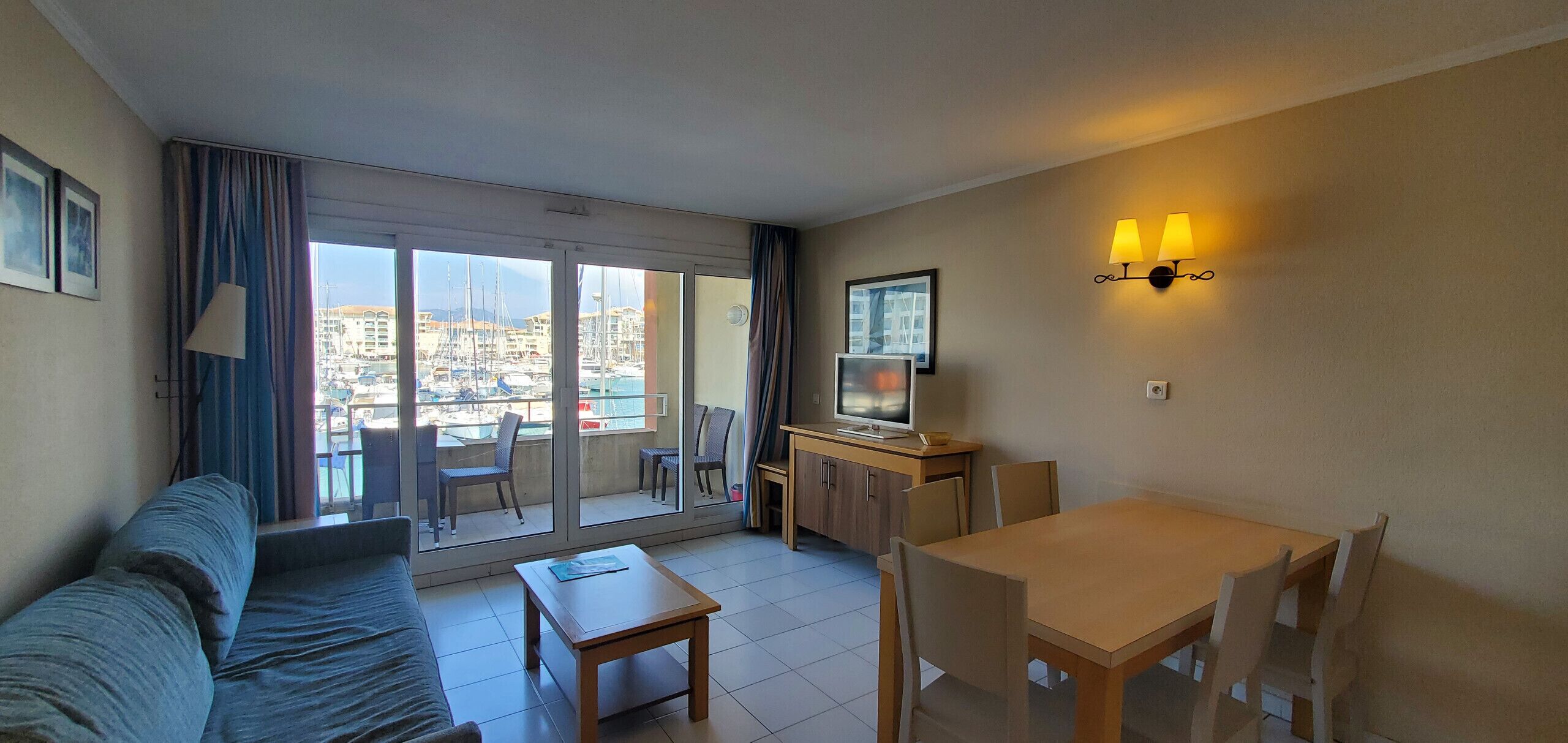 Quarto de hotel com varanda, sofá, mesa de jantar e televisão.