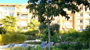 Un hotel con jardín, mesas al aire libre y un edificio de varios pisos con balcones.