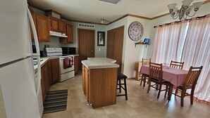 Una cocina con armarios de madera, microondas, estufa y comedor con mesa y sillas.