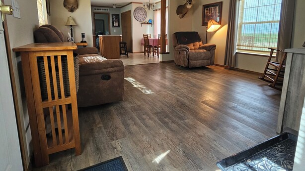 Amplia sala de estar con piso de madera, un sofá marrón, un sillón reclinable y una mesita de madera. Se observan cornamentas de ciervo montadas en las paredes, un candelabro y un comedor al fondo.