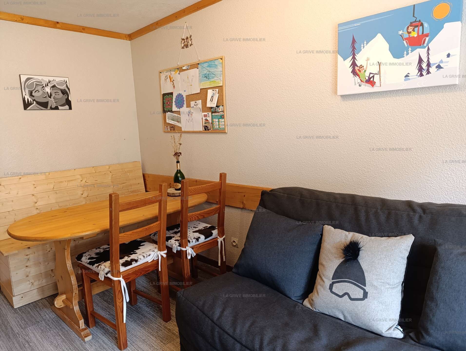 Ein gemütliches Zimmer mit einem Holztisch, zwei Stühlen, einer Couch und einer Pinnwand an der Wand.