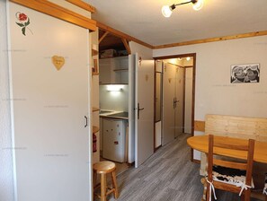 A compact kitchen with a refrigerator, a stove, and a sink. There is a wooden bench and a small stool in the dining area.
